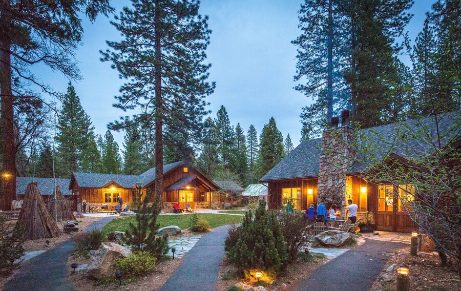 A lodge with multiple cabins, surrounded by tall pine trees, featuring a stone chimney and outdoor seating areas. - Evergreen Lodge Yosemite (Groveland)