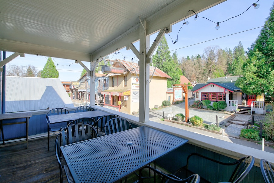 An outdoor patio with metal tables and chairs, a covered area with string lights, and a view of a small town with various buildings. - Hotel Charlotte (Groveland)