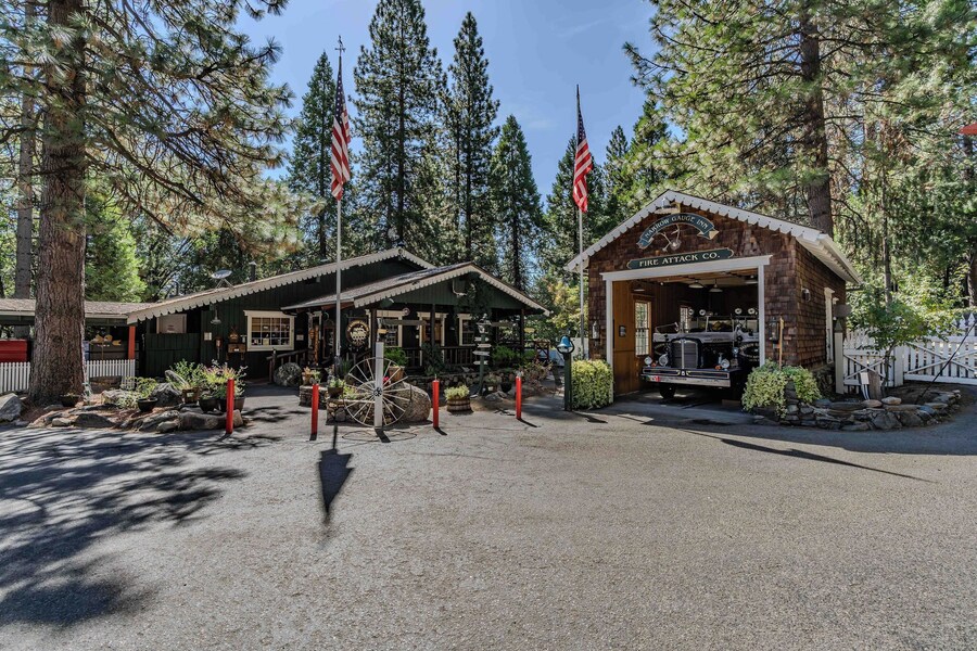 A rustic lodge with a covered porch, a vintage car, and American flags. - Narrow Gauge Inn (Fish Camp)