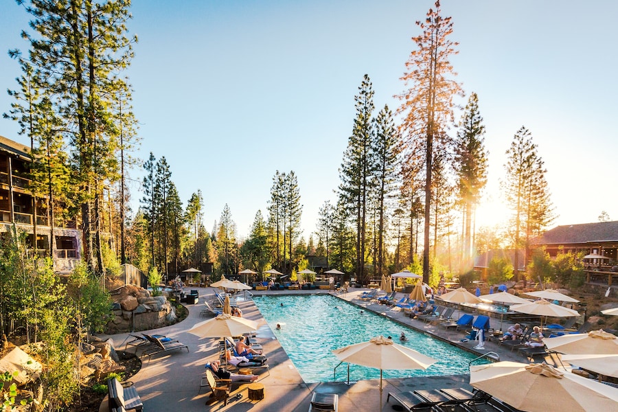 A pool area with lounge chairs and umbrellas, surrounded by tall trees and a building in the background. - Rush Creek Lodge and Spa at Yosemite (Groveland)
