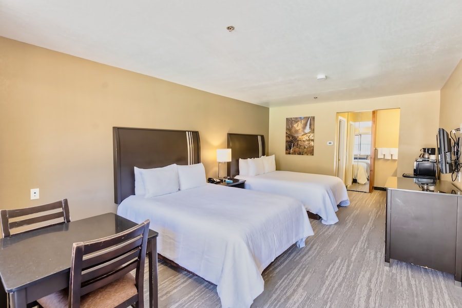 A hotel room with two beds, a desk, a chair, a TV, and a kitchenette. - The Oakhurst Inn at Yosemite (Oakhurst)