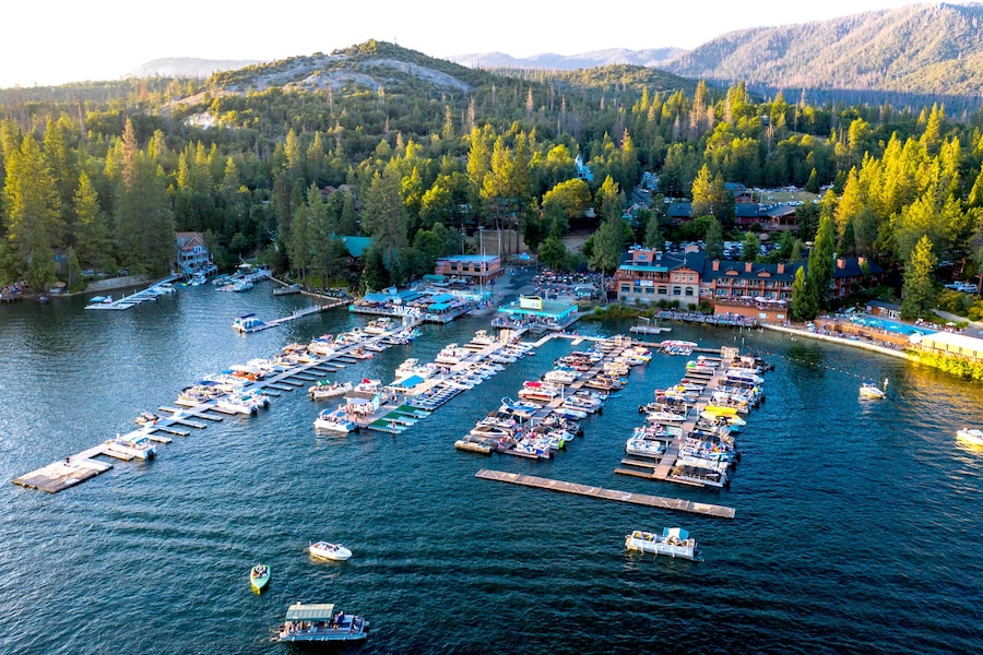 An aerial view of a marina with multiple docks and boats, surrounded by dense forest and mountains. - The Pines Resort (Bass Lake)