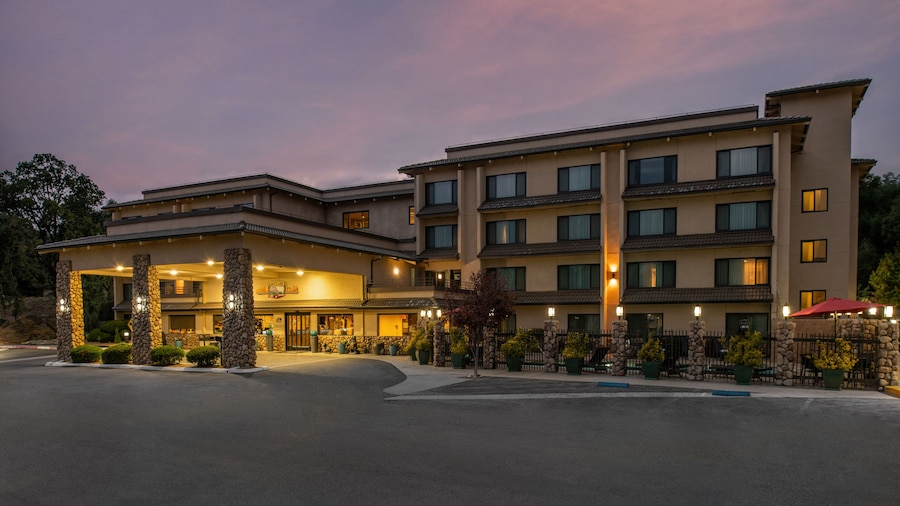 A multi-story hotel with a covered entrance, stone pillars, and a landscaped driveway. - Yosemite Southgate Hotel & Suites (Oakhurst)