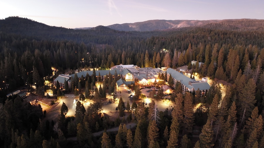 An aerial view of a lodge surrounded by dense forest, with multiple buildings and a parking area. - Tenaya at Yosemite (Fish Camp)